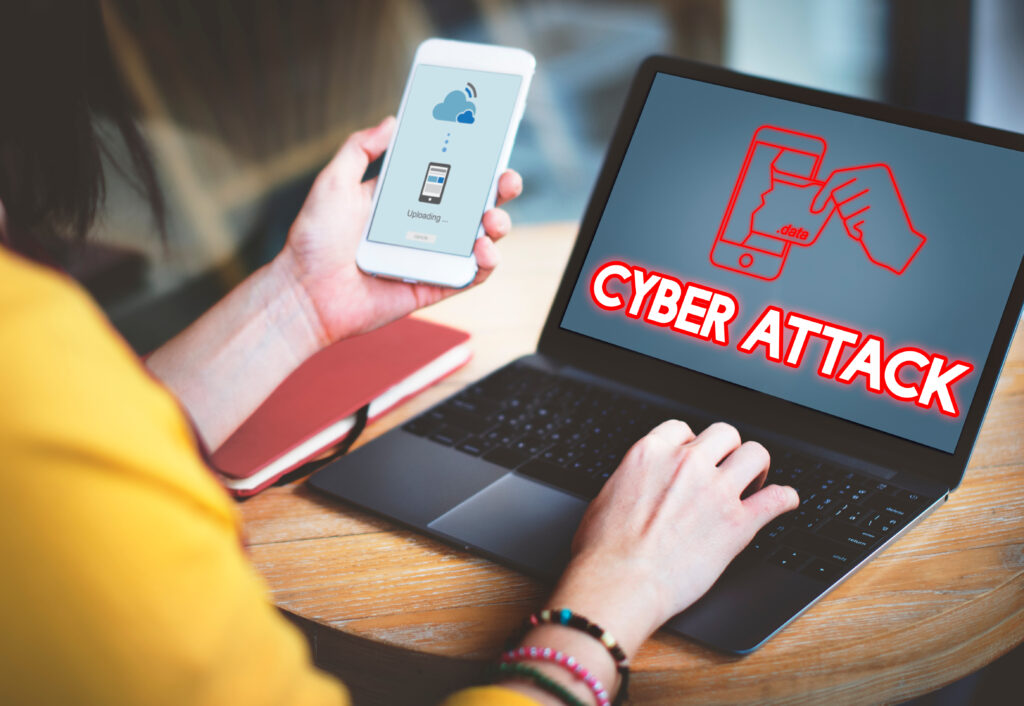 A person working on a laptop with a "CYBER ATTACK" warning