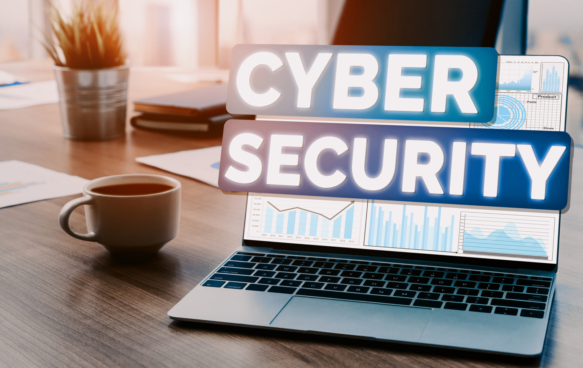 Laptop displaying charts with “Cybersecurity” text overlay, next to a coffee cup on a desk
