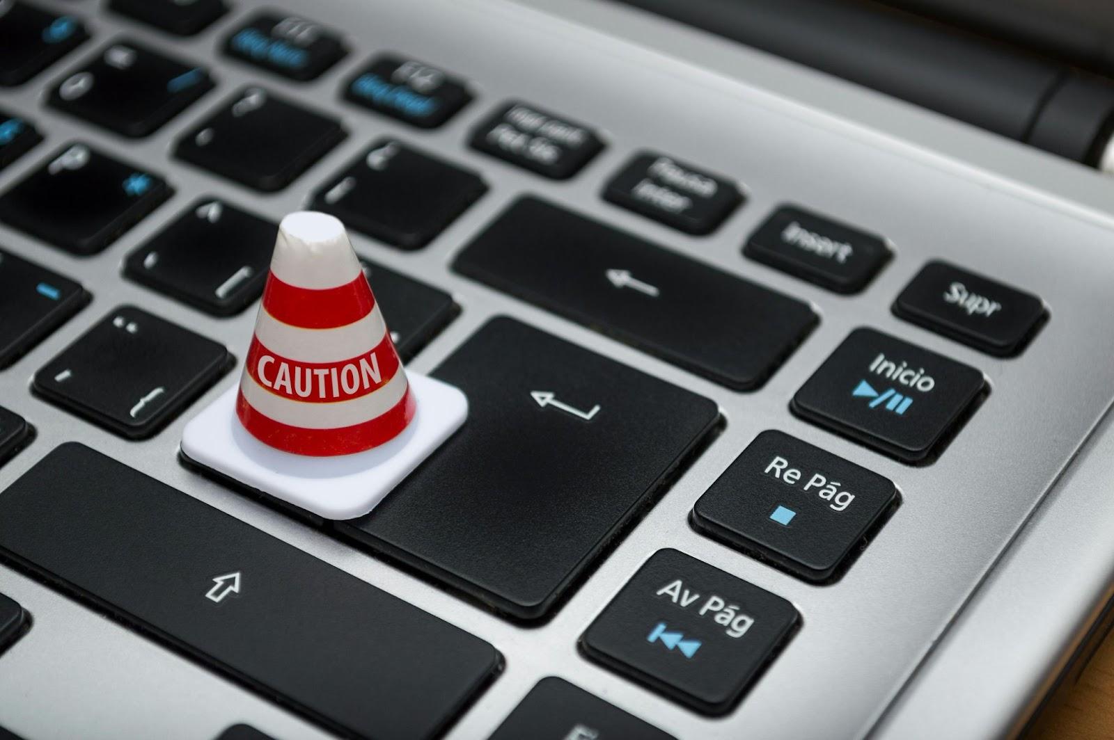 Small caution cone placed on a laptop keyboard, symbolizing digital risks