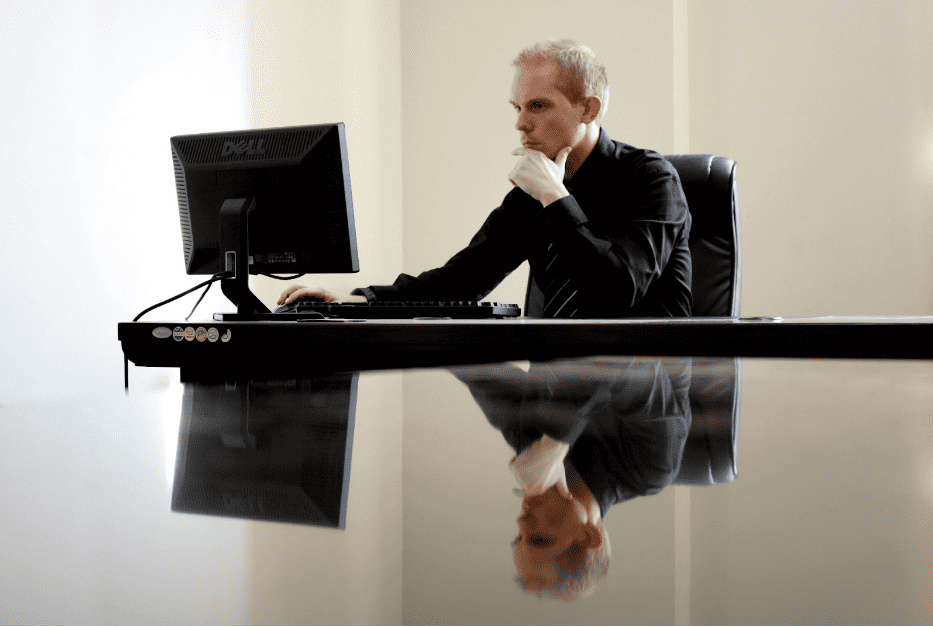 A businessman looks at the screen of his computer while deep in thought. 