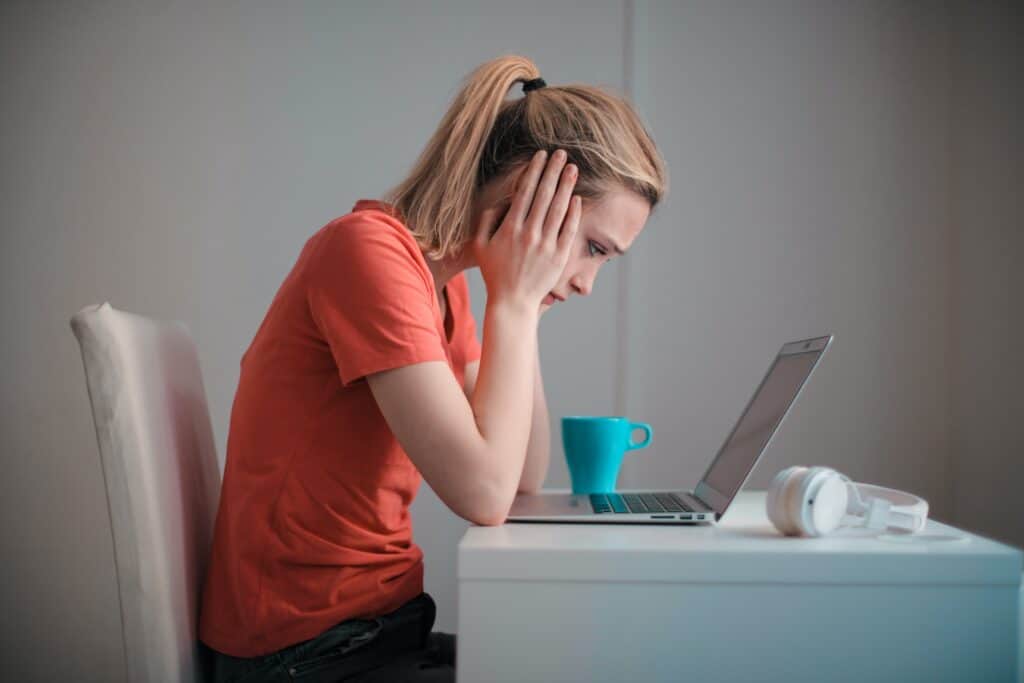 A troubled employee with her face in her hands looks at her laptop as she experiences IT issues.