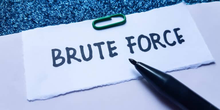 Torn white note reading 'BRUTE FORCE' on a blue textured surface, with a green paperclip and a black pen nearby.