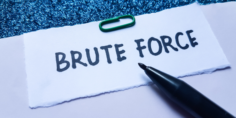 Torn white note reading 'BRUTE FORCE' on a blue textured surface, with a green paperclip and a black pen nearby.