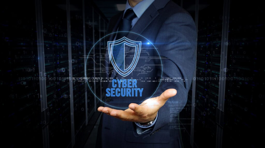 A businessman in a suit holds a virtual screen with a cybersecurity shield hologram.