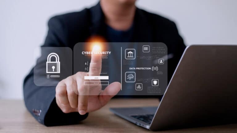 A man touches a screen with "cybersecurity" written on it, with a laptop in the background.