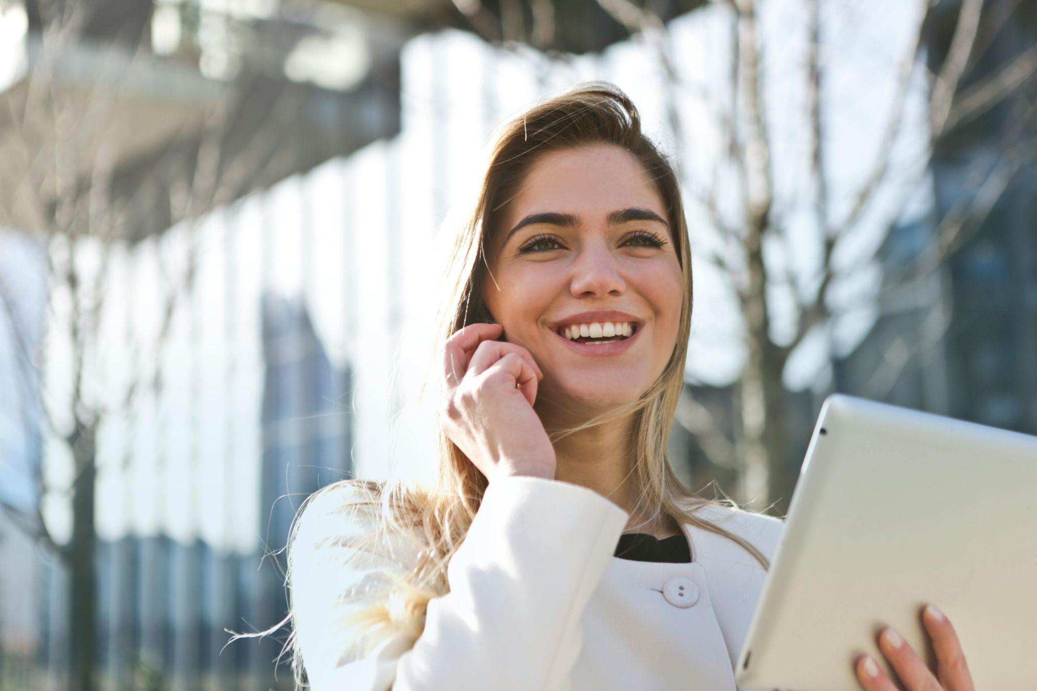 A woman talks over the phone and smiles while holding a laptop