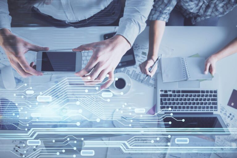 Top-down view of a Tampa business team collaborating at a desk with laptops and smartphones, overlaid with blue digital circuit and data icons representing managed IT services and cybersecurity.
