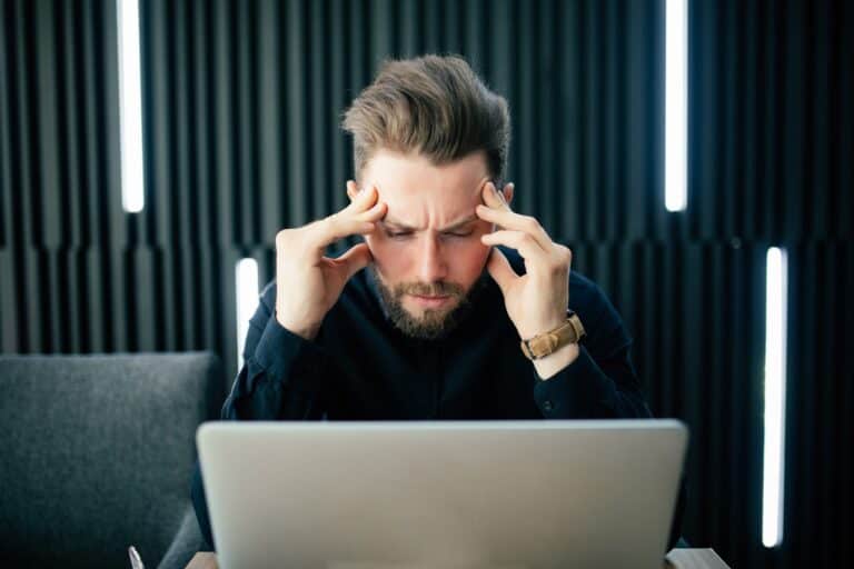 A business owner rubs his temples as he looks at a data breach on his laptop.