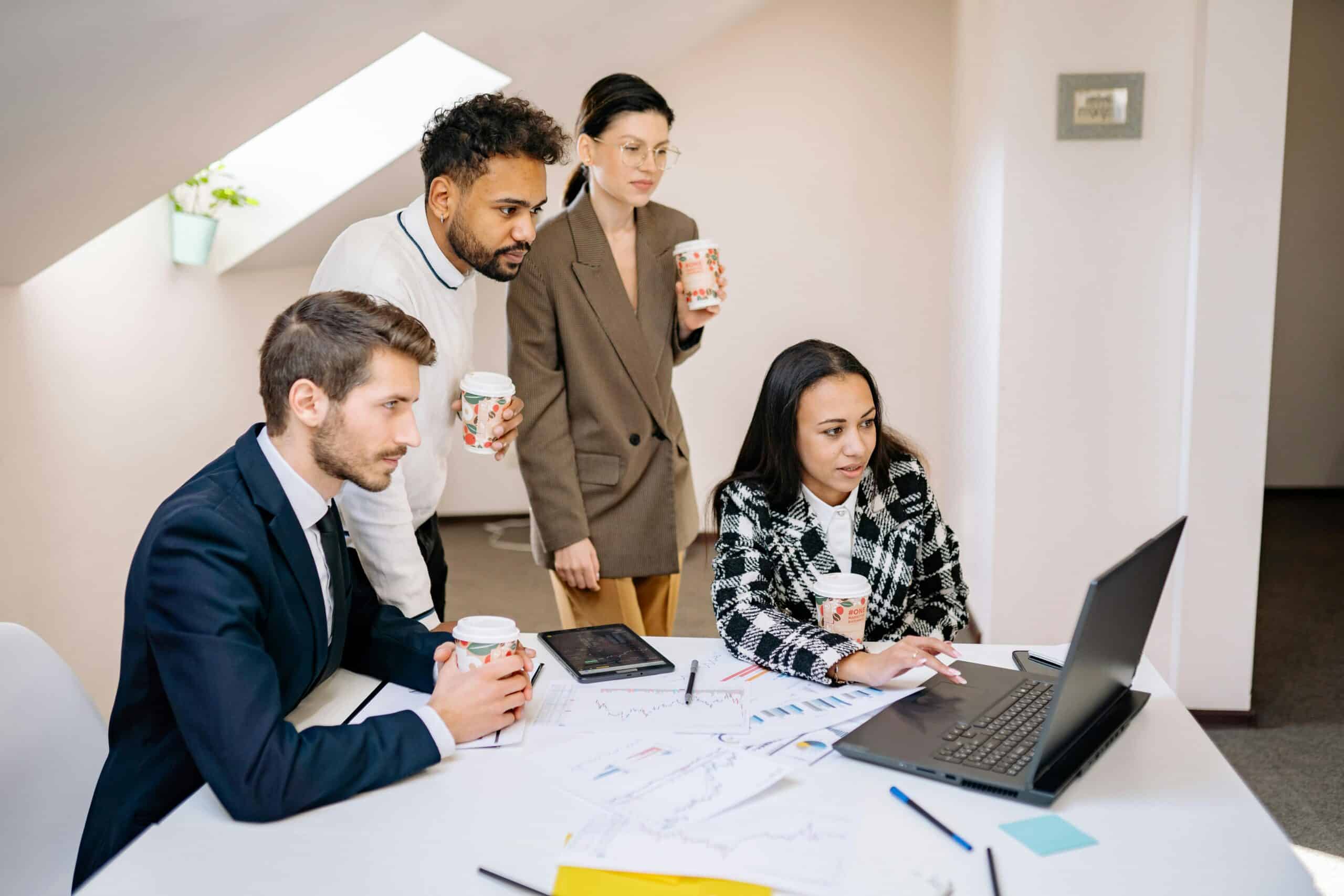 A group of businessmen and women look towards the laptop while working.