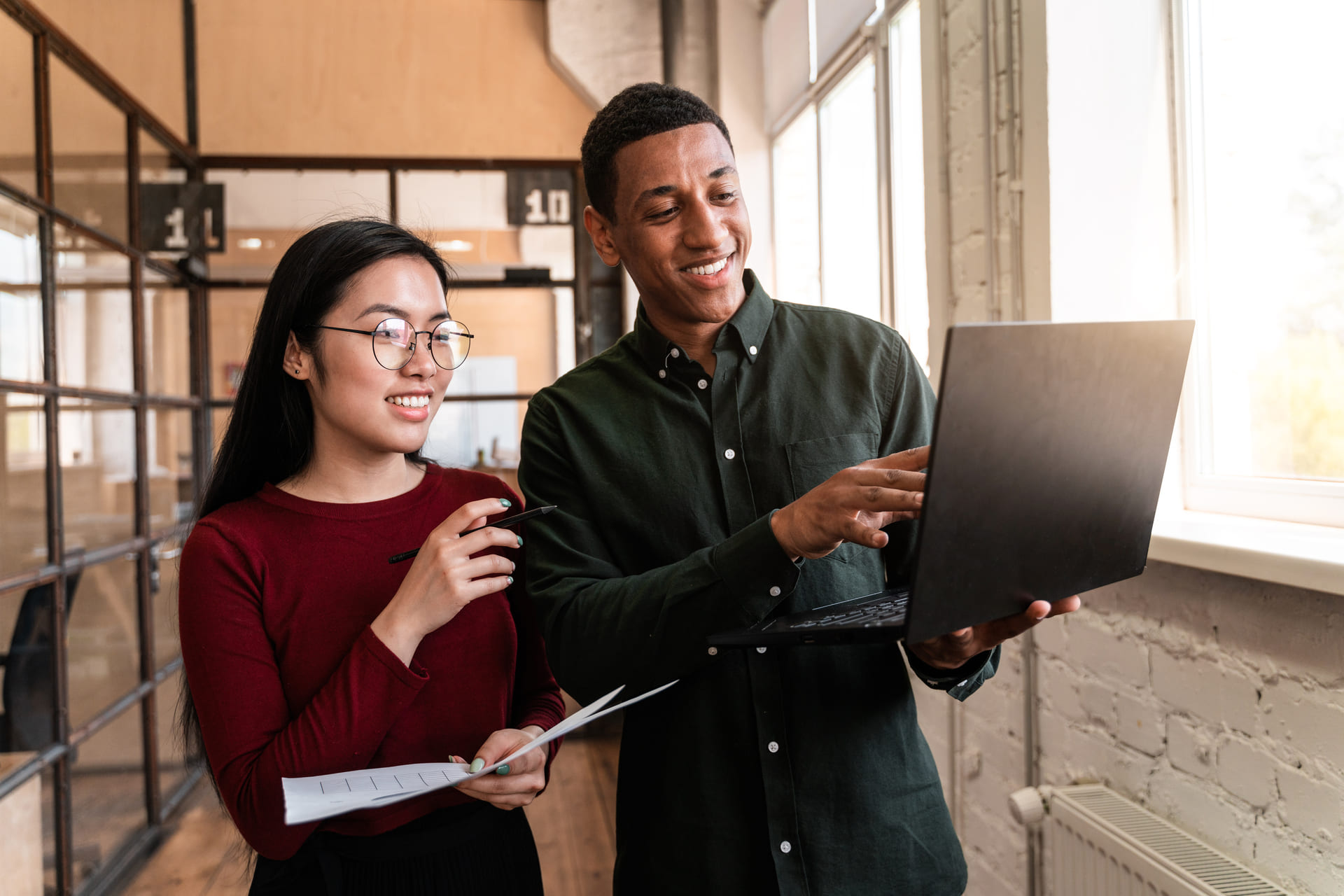 Two colleagues collaborating and discussing work while using a laptop