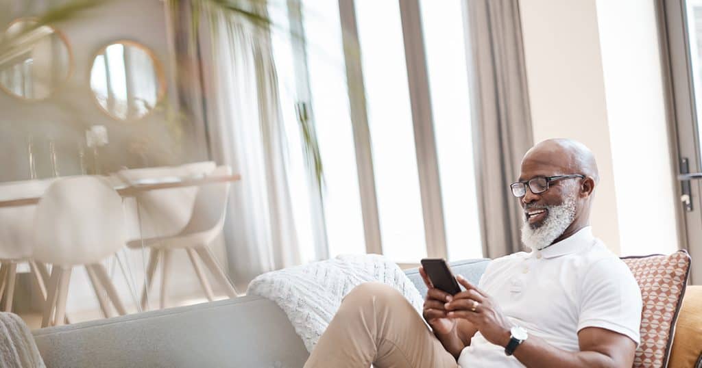 African American man sitting on couch scrolling through phone
