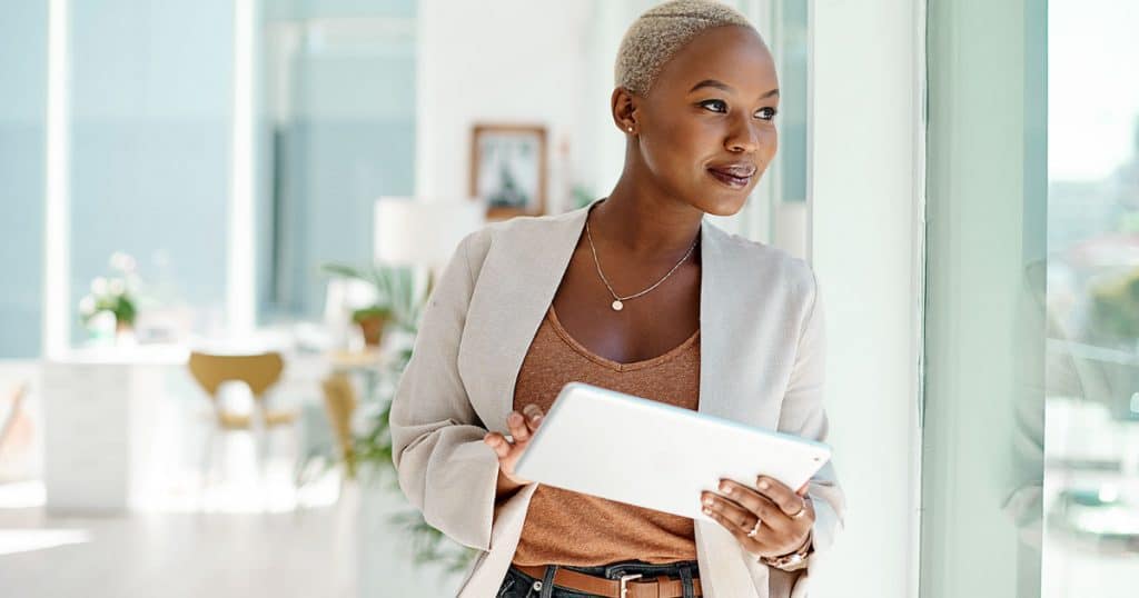 young black young businesswoman using a digital tablet while looking out the window in an office