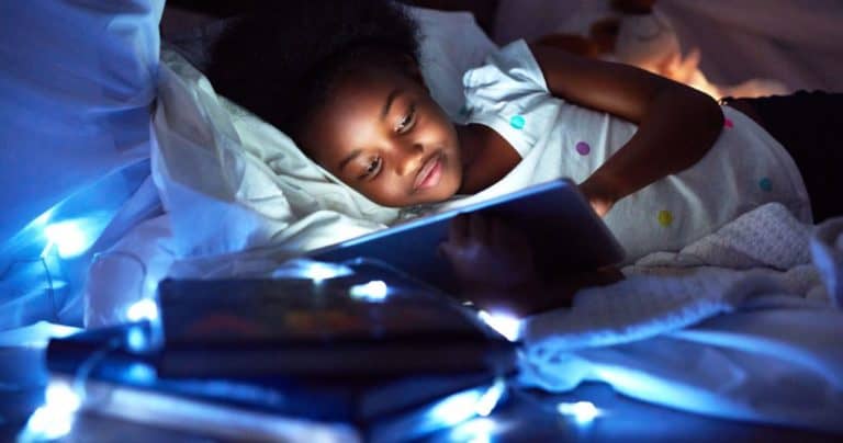young girl looking at tablet under a pillow fort with string lights