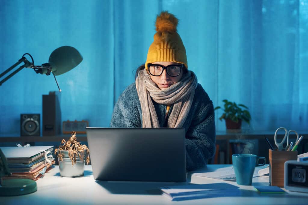 Woman sitting at desk and feeling cold, she is wearing warm clothes and protecting her data.