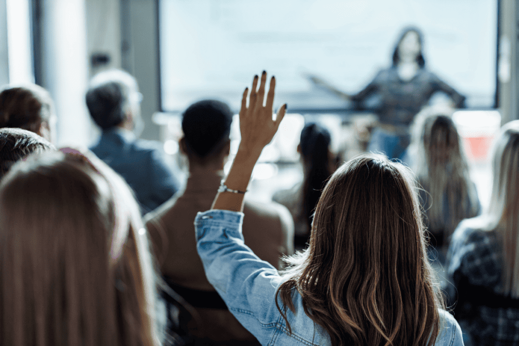 Woman raises her hand while sitting through a presentation.