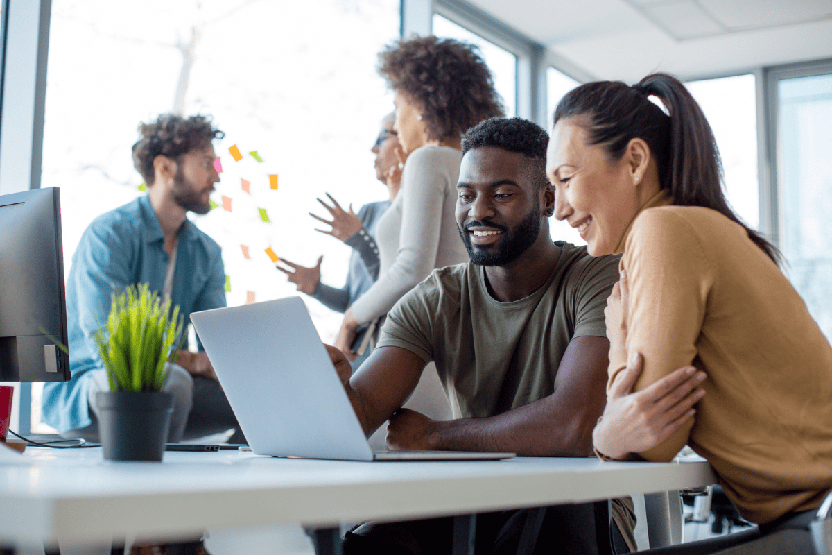 co-workers sit at desk looking at a laptop