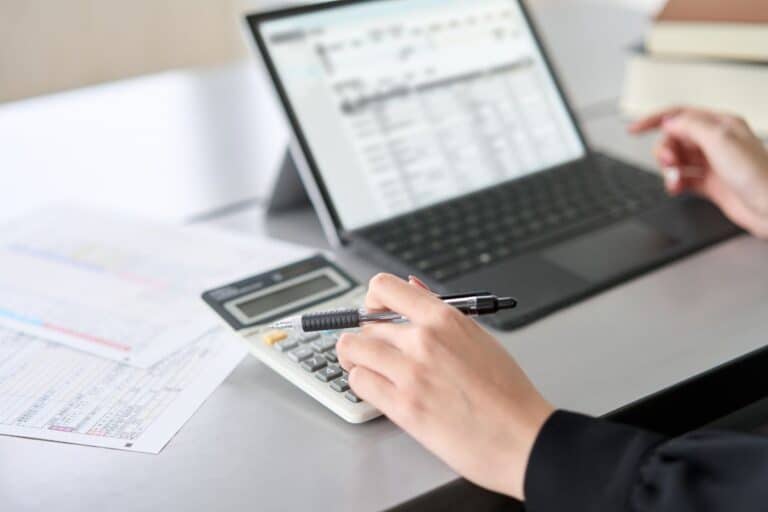 Close-up of a person using a calculator and reviewing tax documents on a laptop, highlighting cybersecurity best practices for the 2025 tax season.