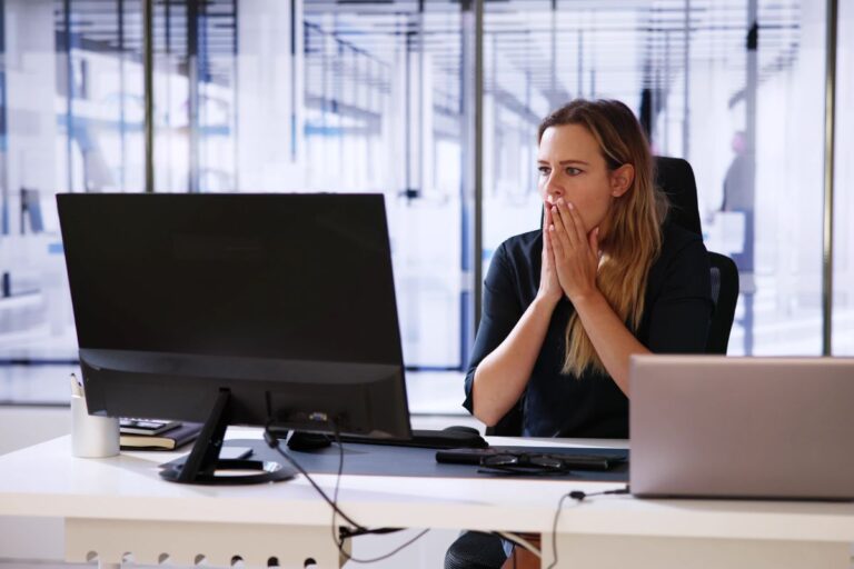 Concerned businesswoman looking at her computer screen, representing the shock and risks of data breaches and cybersecurity threats in the workplace
