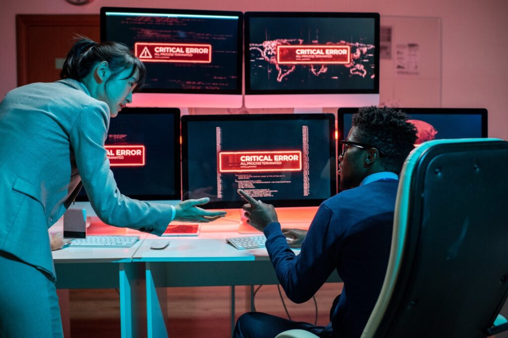 Two IT specialists discussing a critical error alert on multiple computer screens