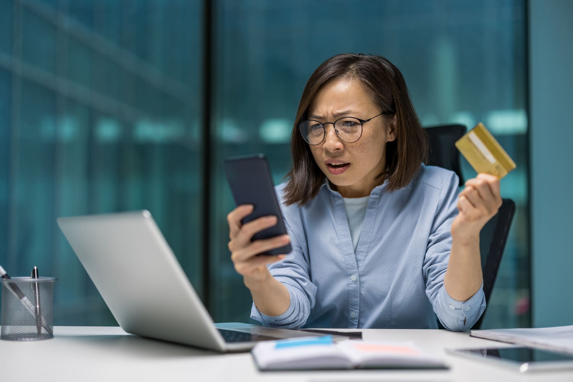 Confused woman holding credit card and looking at smartphone