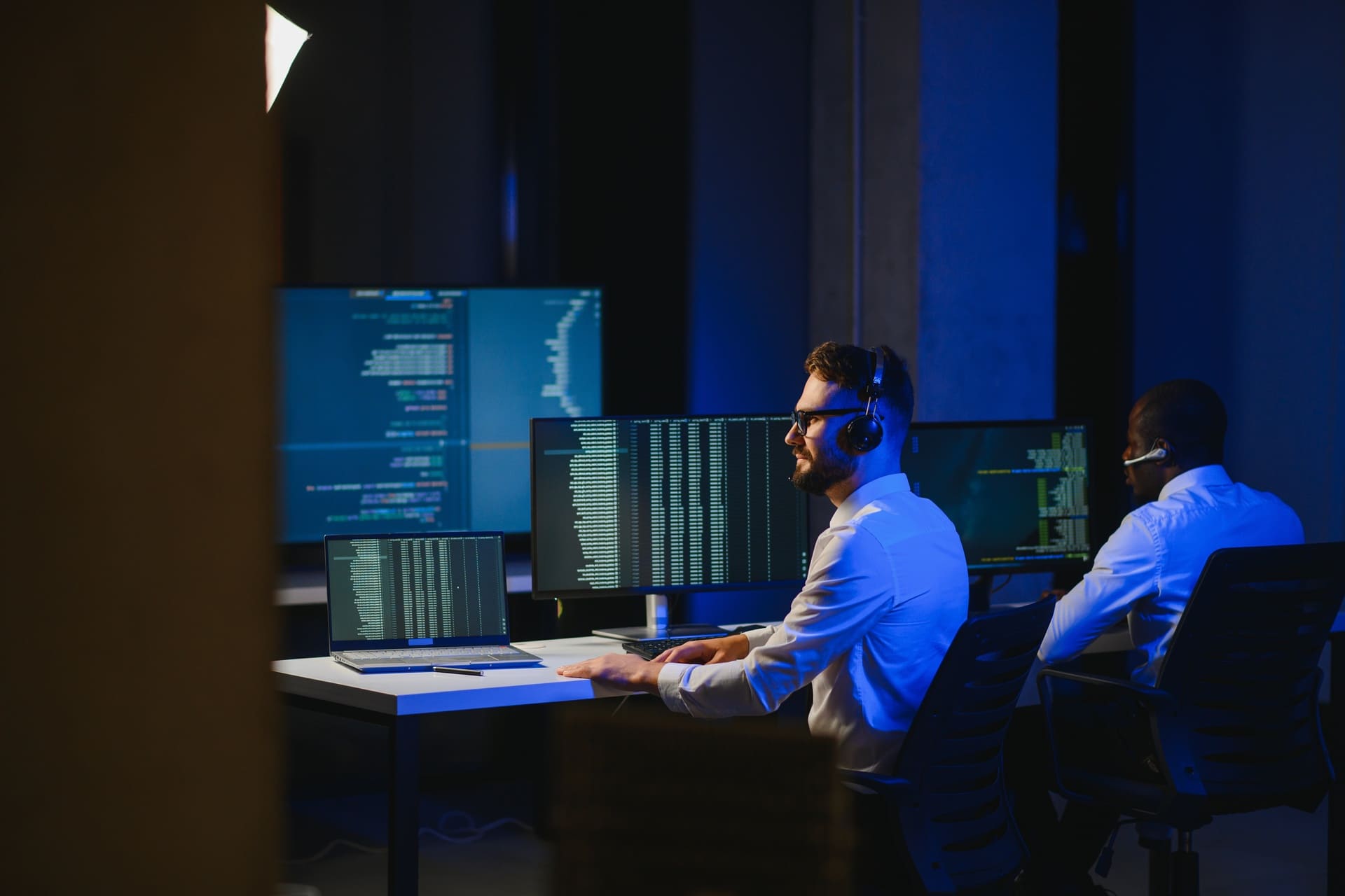 Cybersecurity specialists working at multiple computer screens in a dark operations room