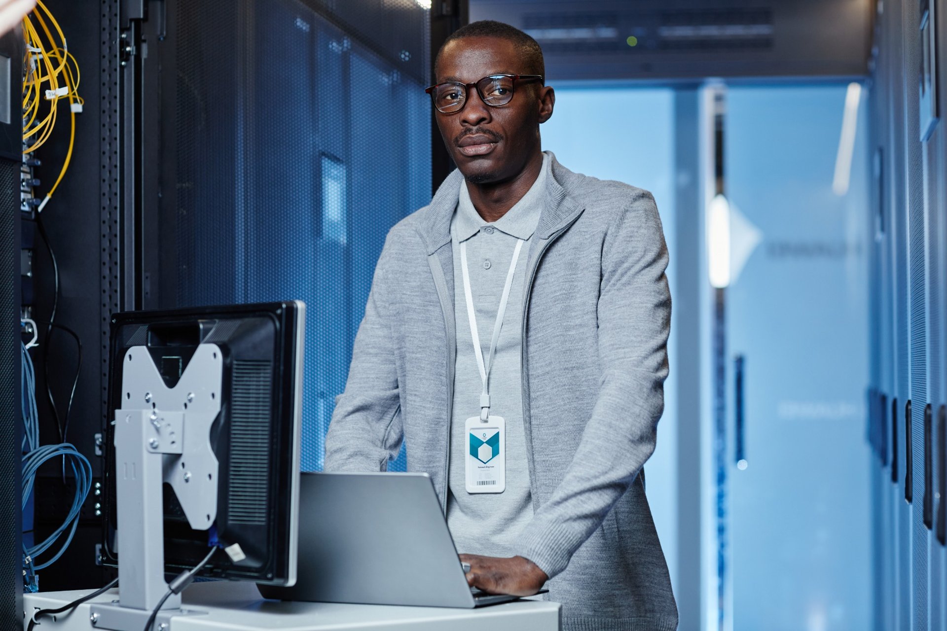 IT professional standing in a server room with a laptop and identification badge