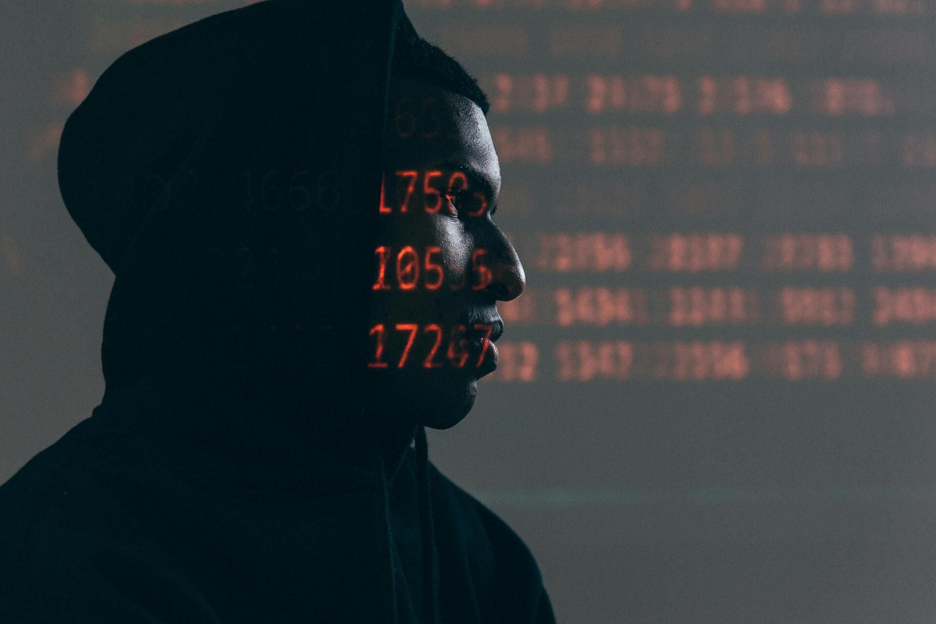 Network Security Threats - Man in hoodie with red data projection on face