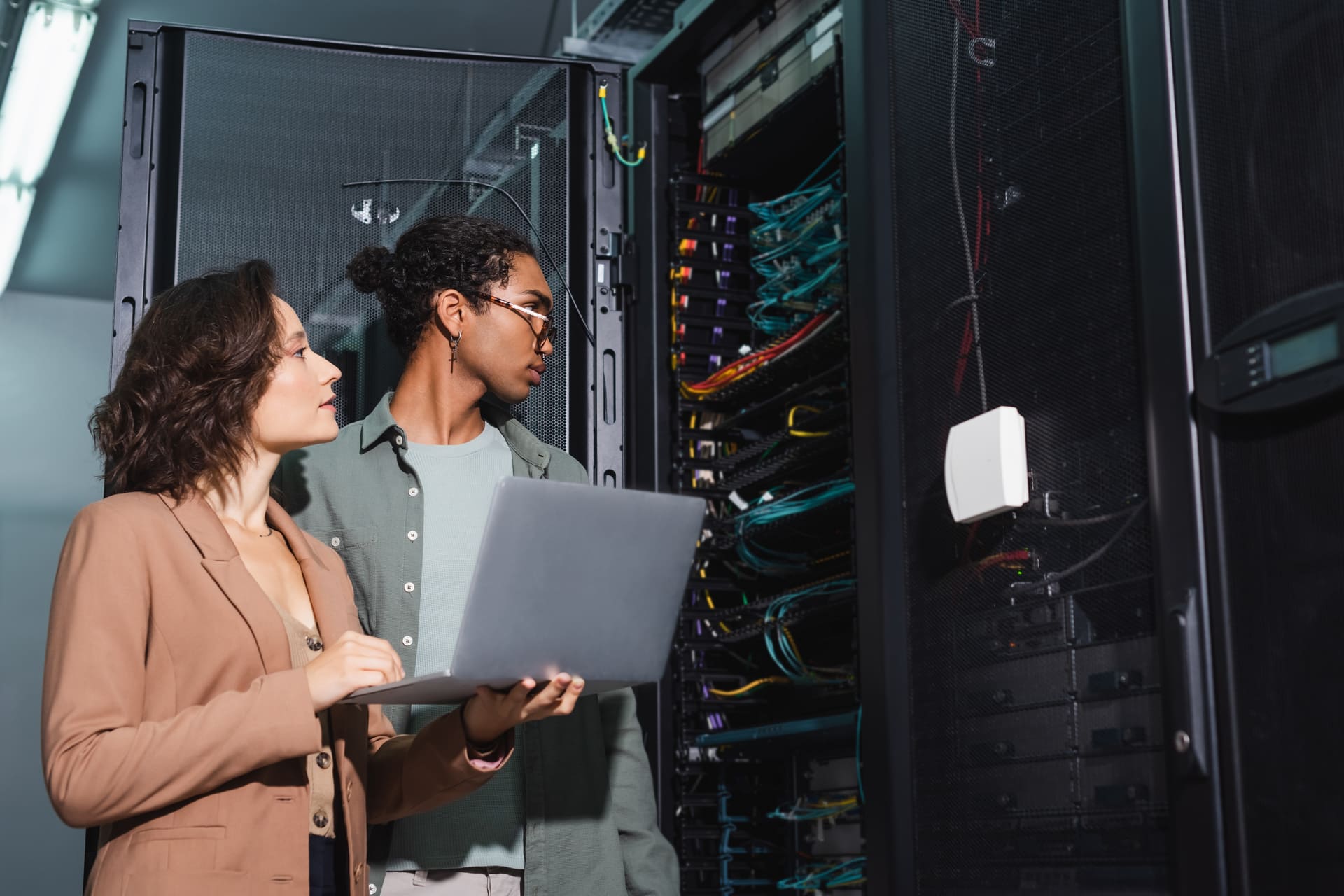 Two engineers analyzing server racks with a laptop in a data center