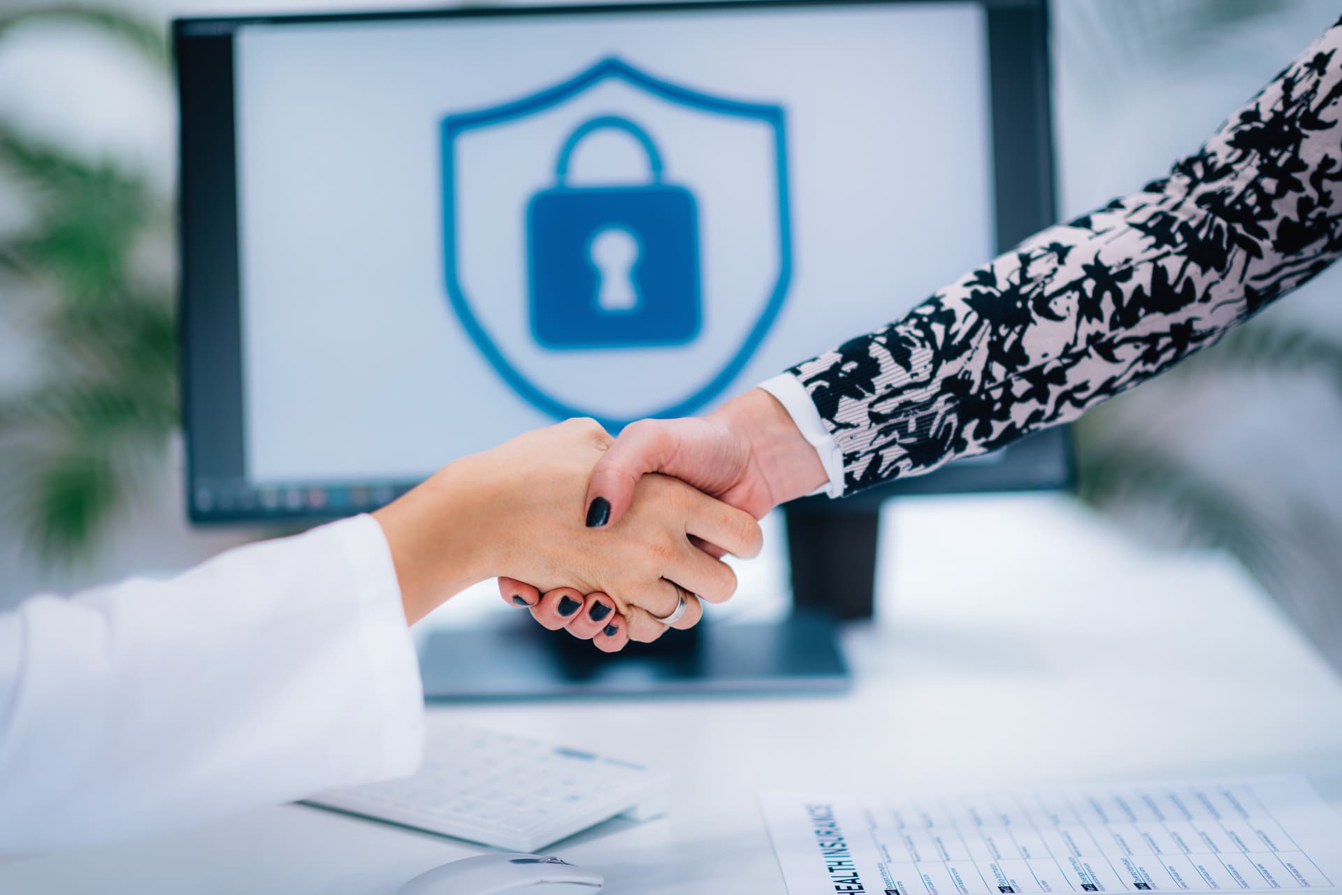 Two people shaking hands in front of a screen displaying a cybersecurity lock icon