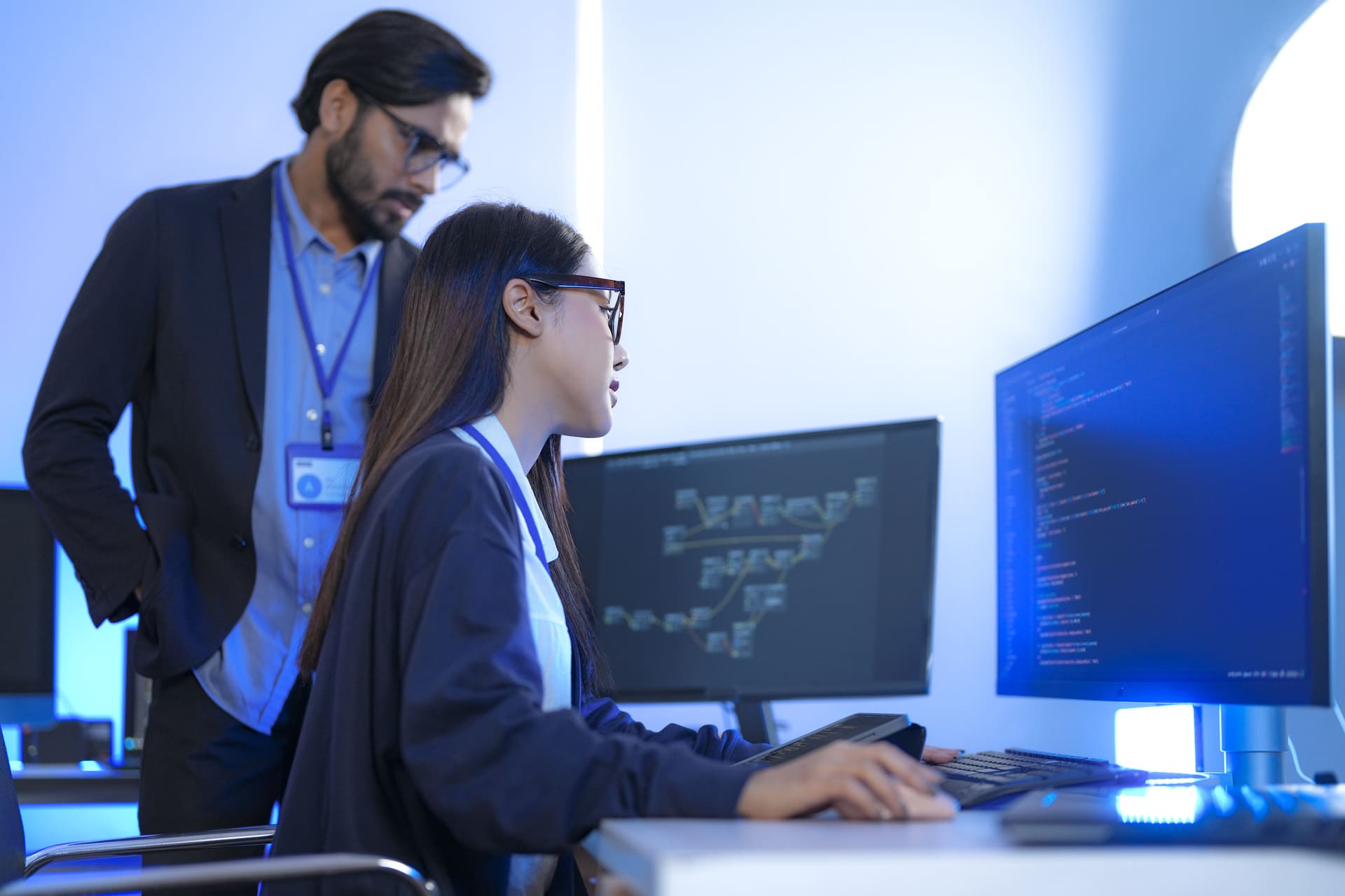 Woman working on computer code while a colleague supervises in an office