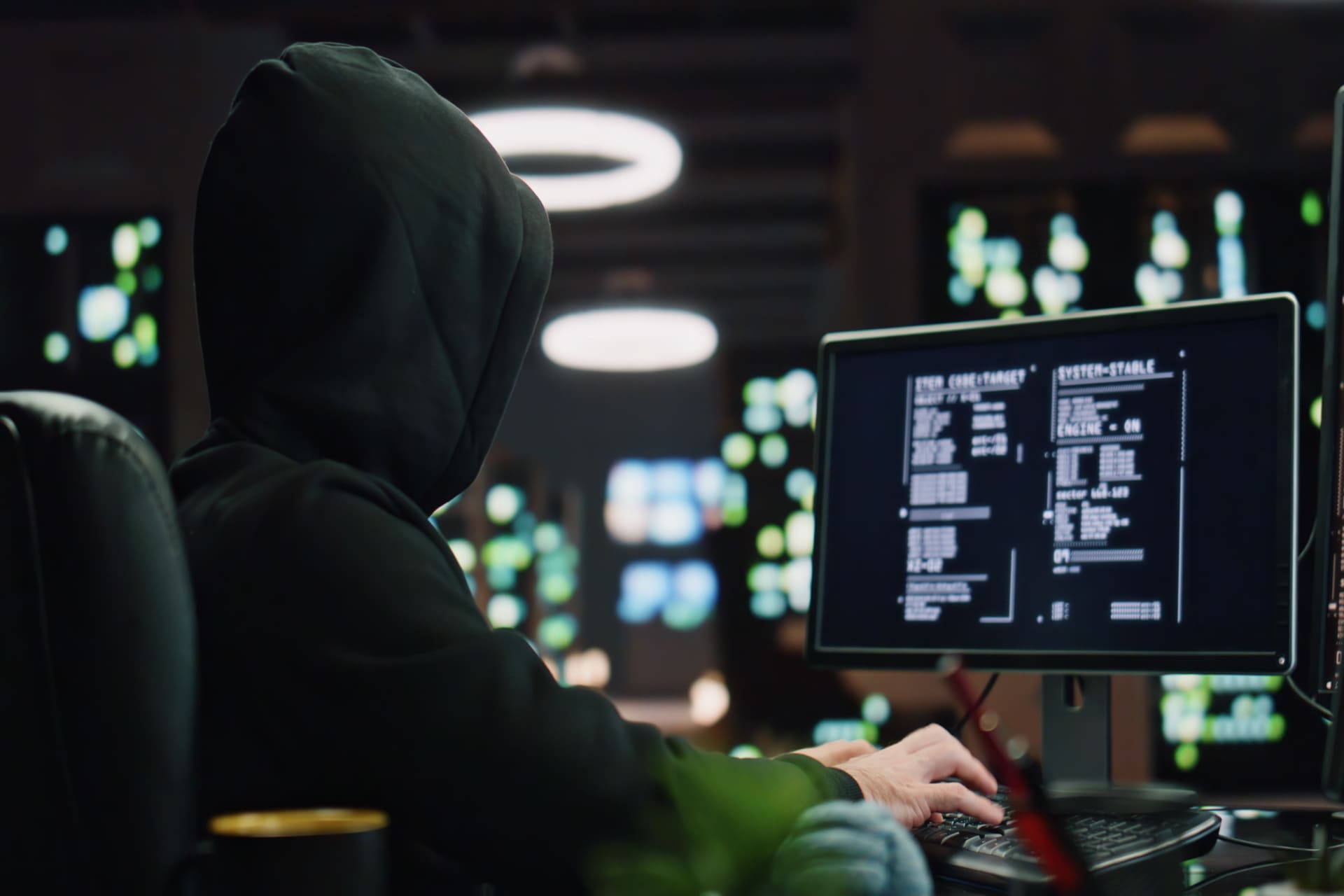 Hooded hacker working at a computer in a dark room