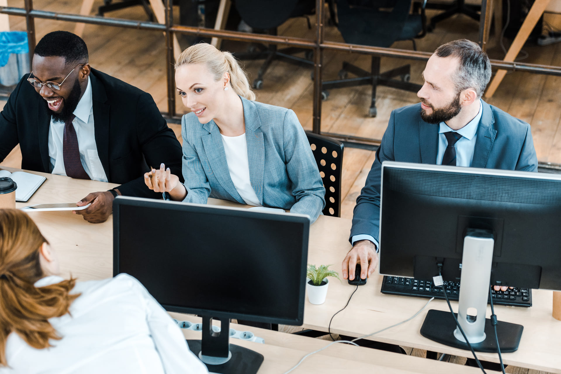 Business colleagues discussing work at office desks with computer monitors