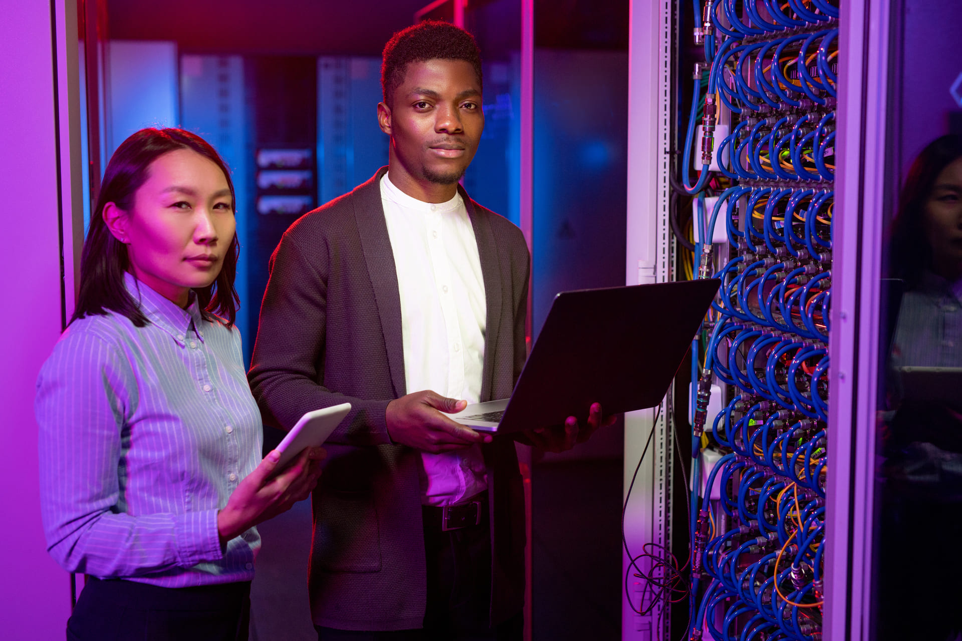 IT engineers standing by server rack with laptop and tablet