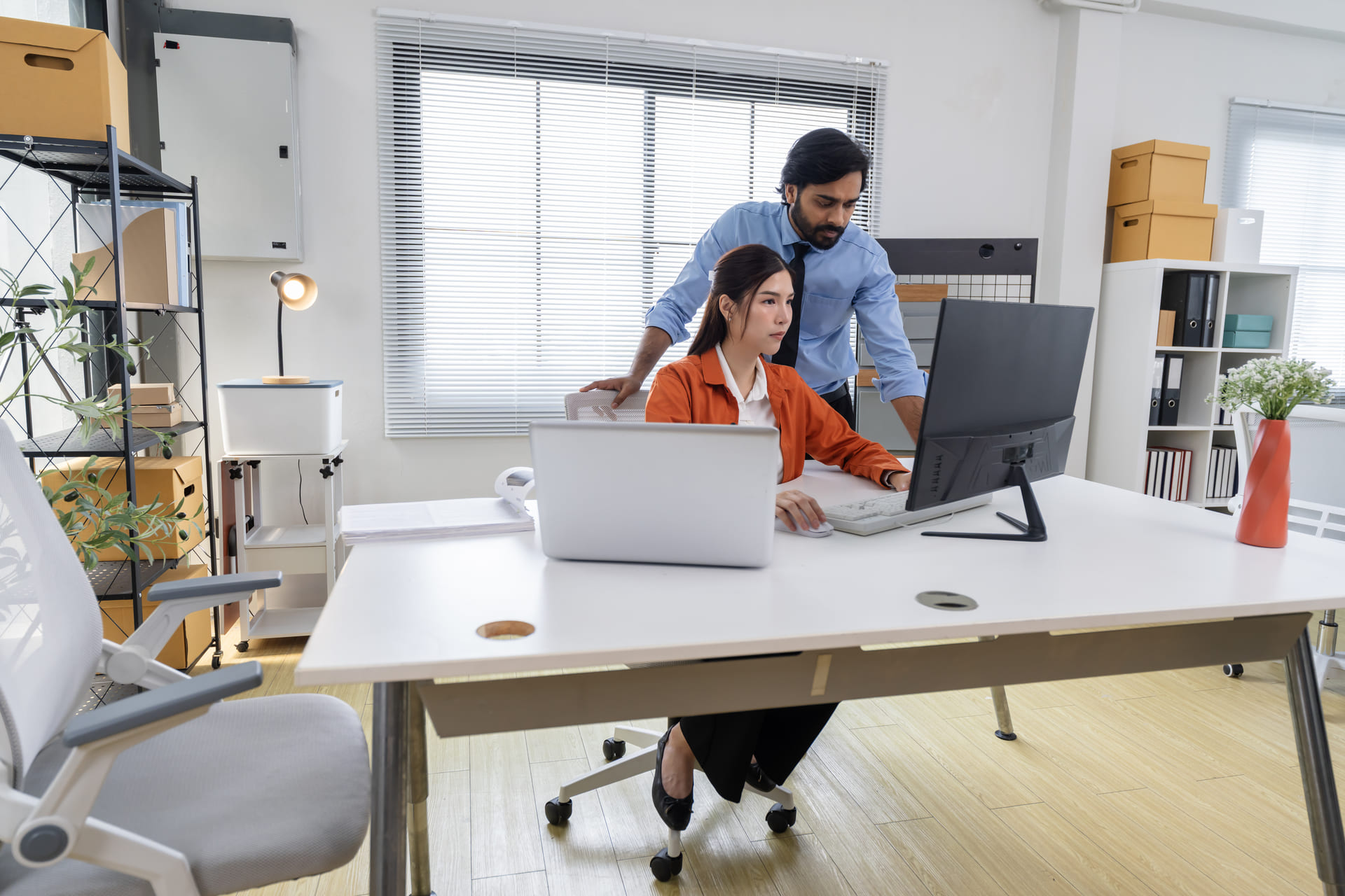 Man assisting woman working on desktop computer in bright office