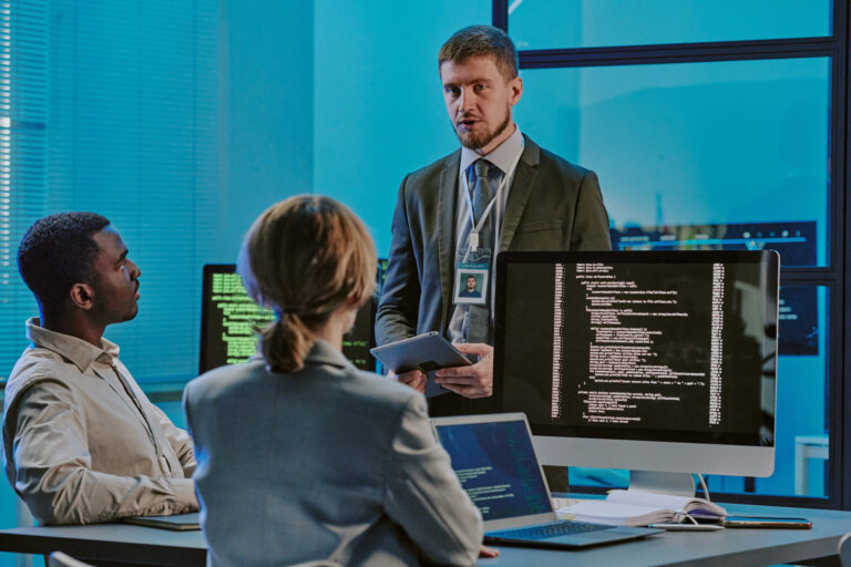 Cybersecurity team meeting around computers with code on screens