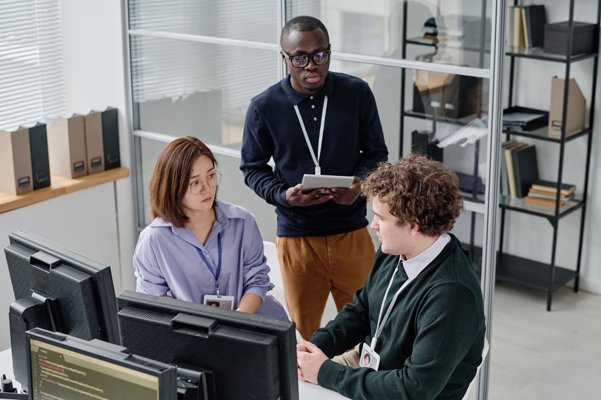 Small team discussing work at desks one person holding a tablet while others look at monitors | CMIT Solutions Small team discussing work at desks one person holding a tablet while others look at monitors