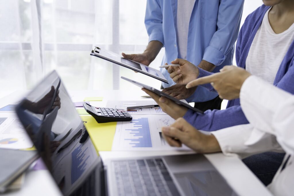 Team members reviewing reports and data on tablets and paper charts during a meeting