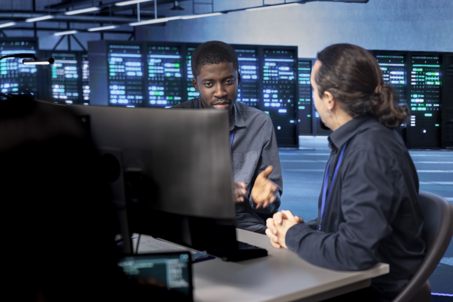 system-administrators-reconfiguring-server-room | CMIT Solutions Two IT professionals in a data center discuss at a desk with server racks in the background.