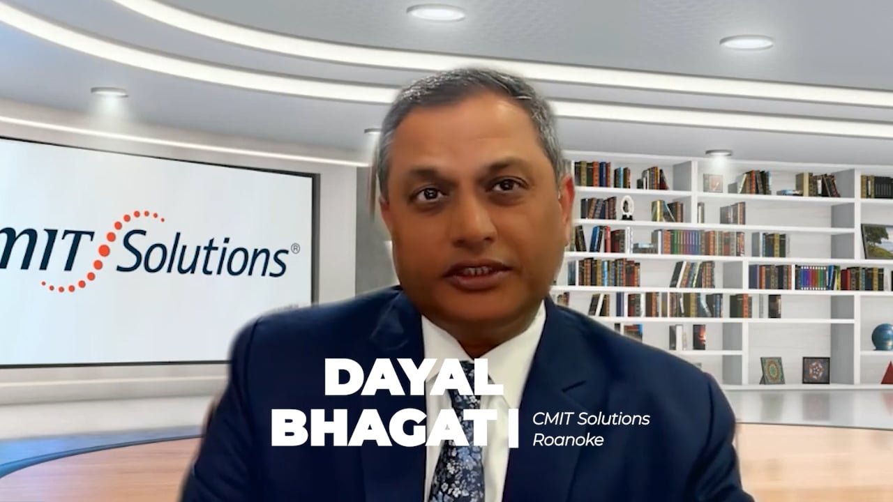 Close-up of Dayal Bhagat in a studio setting with the CMIT Solutions Roanoke logo in the background and a bookshelf scene behind him.