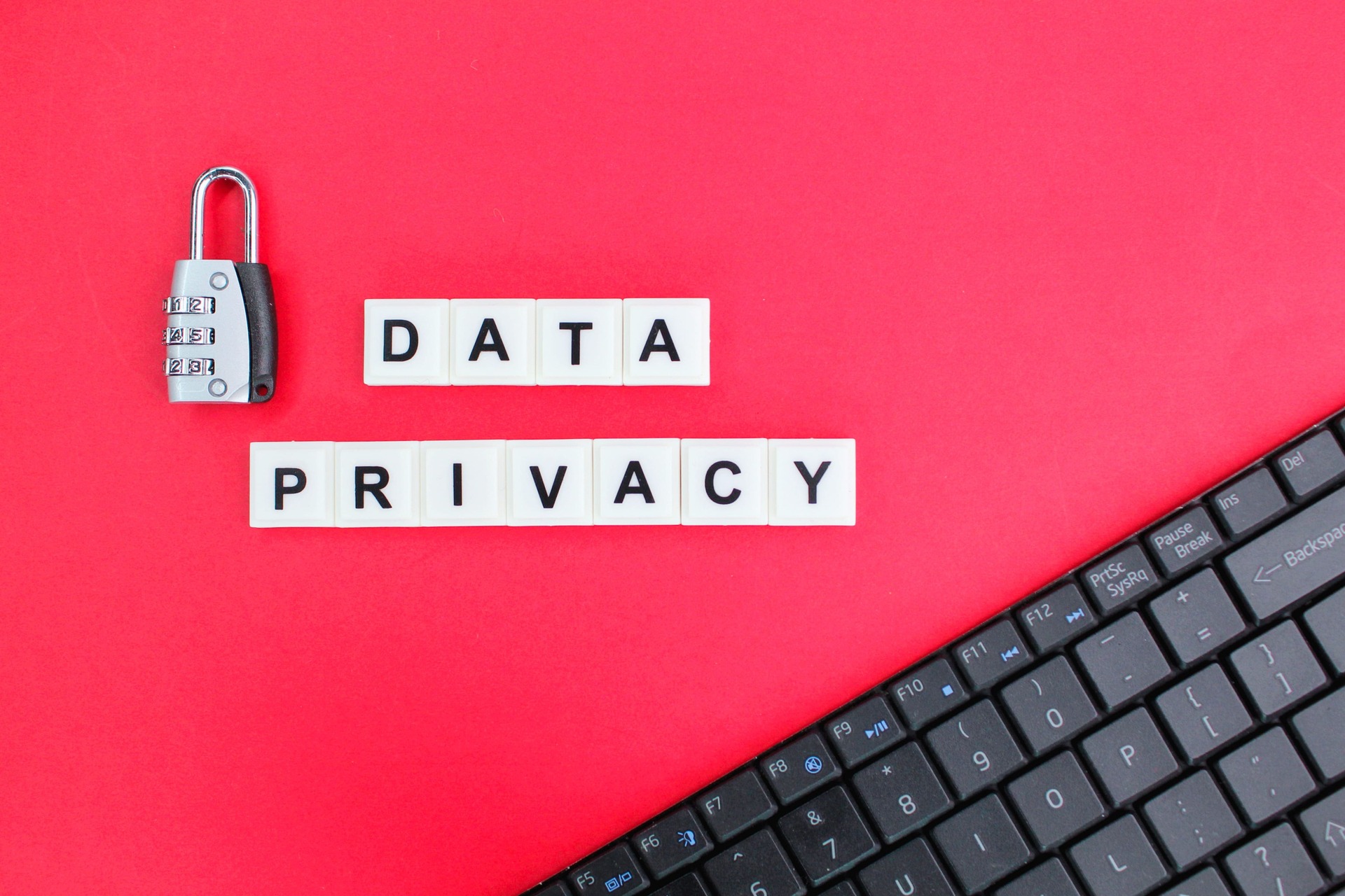 Data privacy text with a padlock and keyboard | CMIT Solutions Padlock beside letter tiles spelling DATA PRIVACY on a red background with part of a keyboard visible on the right edge. visually communicates data security/privacy.