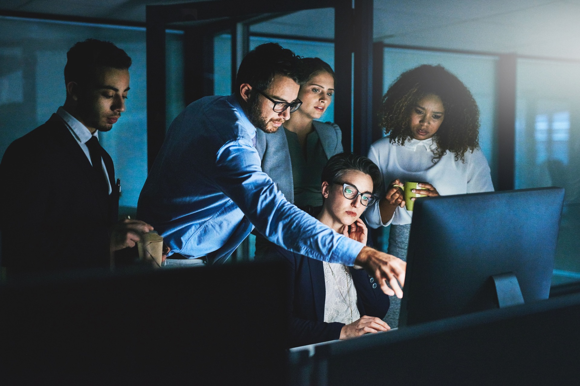 Team collaborating on a computer in a dark office | CMIT Solutions Team collaborating on a computer in a dark office