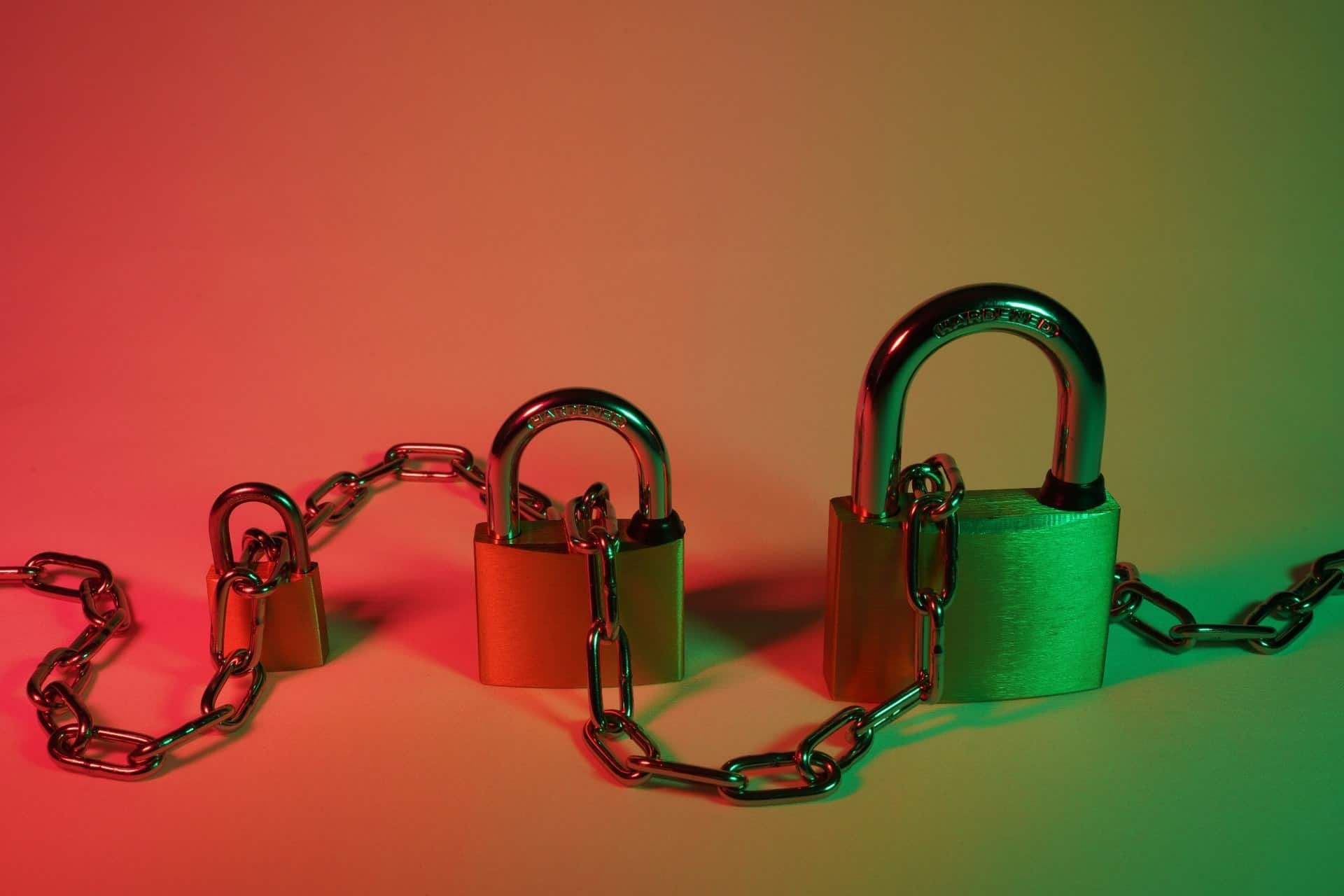 cybersecurity-padlocks-chain | CMIT Solutions Metal padlocks connected by a heavy chain under red and green lighting, representing cybersecurity and data protection.