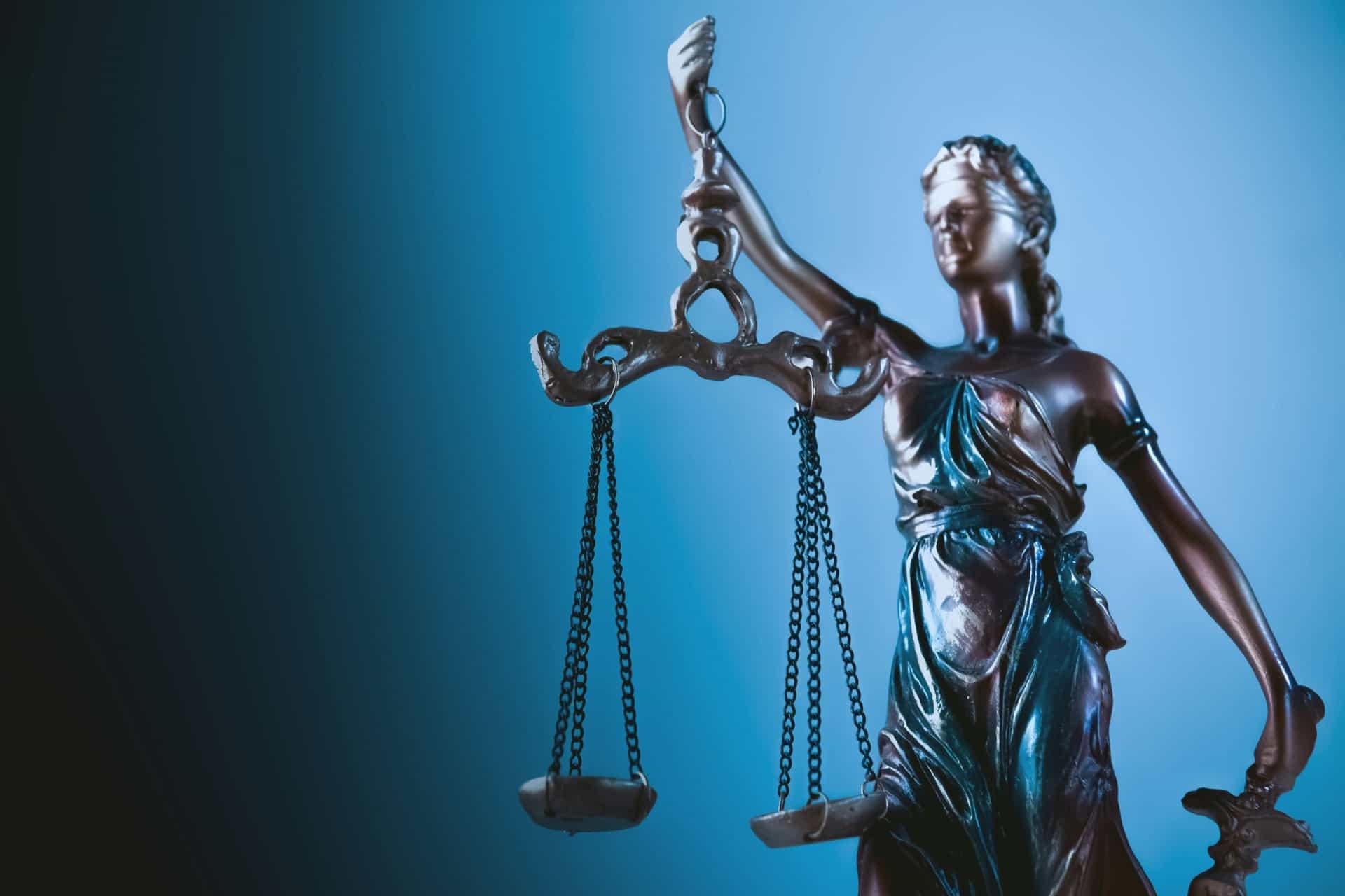 justice-scales | CMIT Solutions Statue of Lady Justice holding balanced scales against a blue gradient background, symbolizing law and fairness.