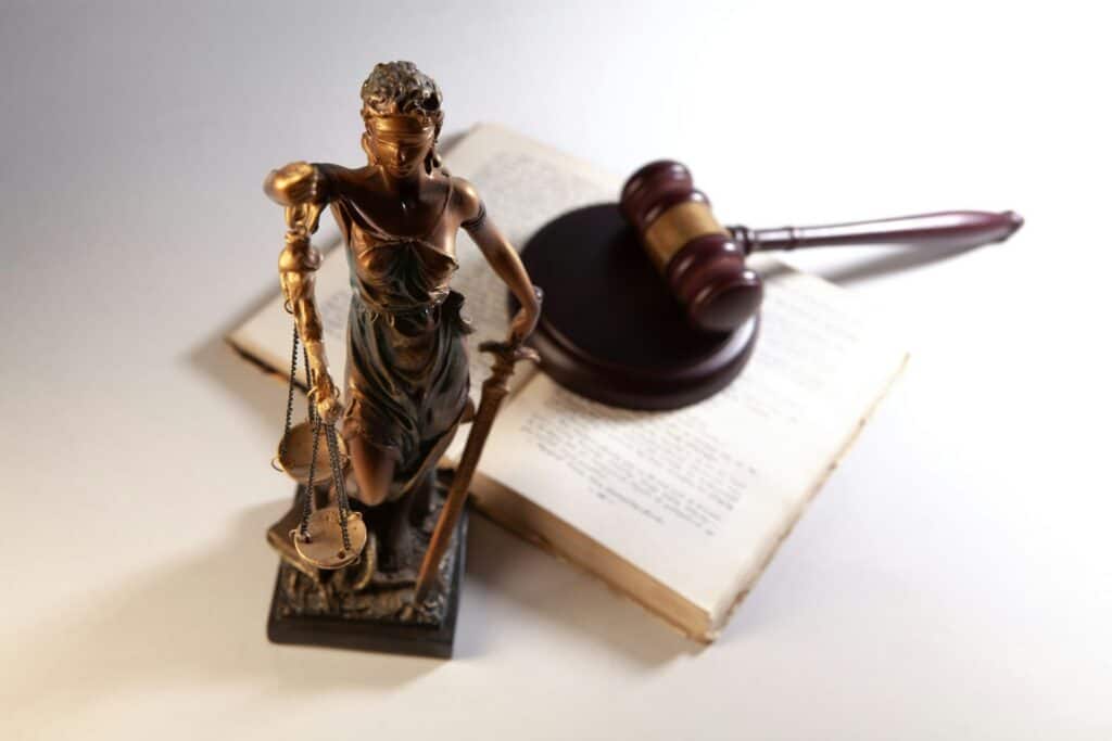 Bronze Statue of Lady Justice holding scales, standing on an open book with a judge's gavel nearby
