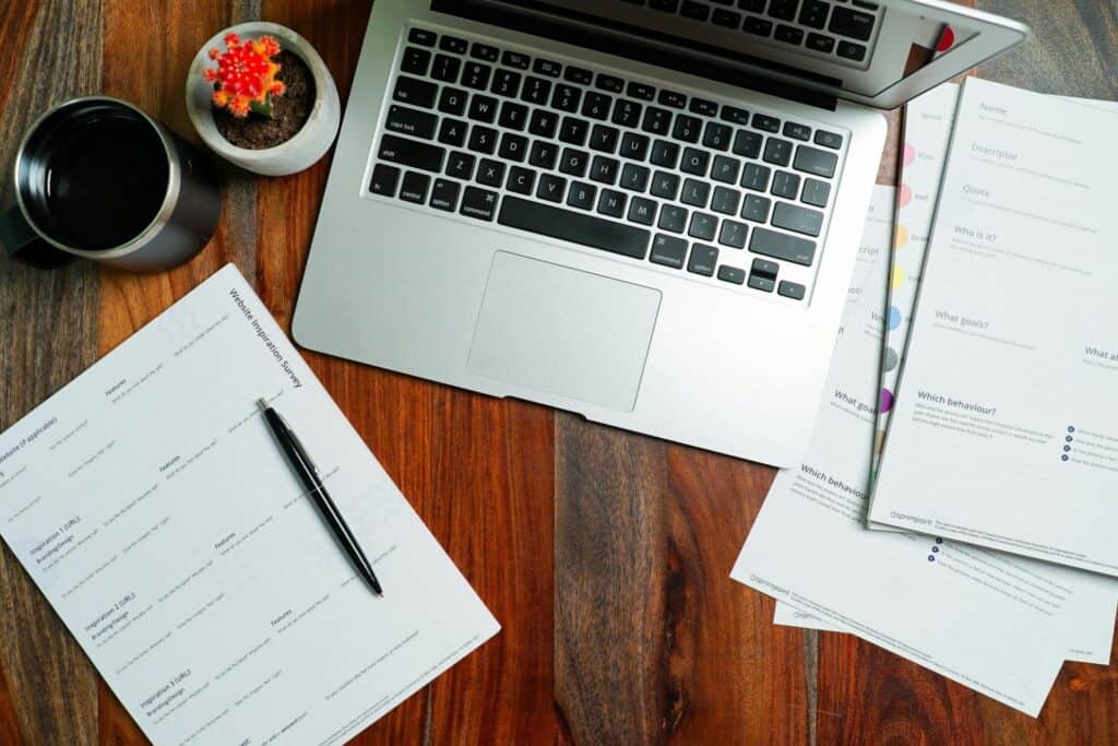 Laptop, planning worksheets, and coffee on a wooden desk.